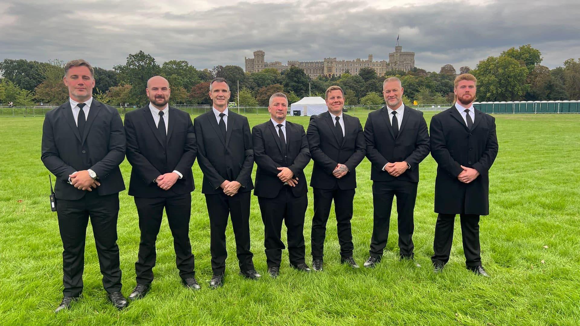 The K1 team in black suits on a lawn, with Windsor Castle behind them
